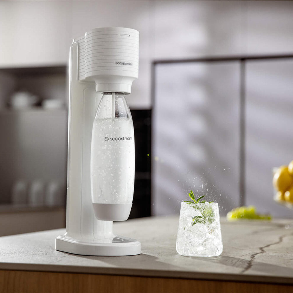 Gasatore d'acqua SodaStream Gaia bianco in ambiente cucina con bottiglia e bicchiere di acqua frizzante